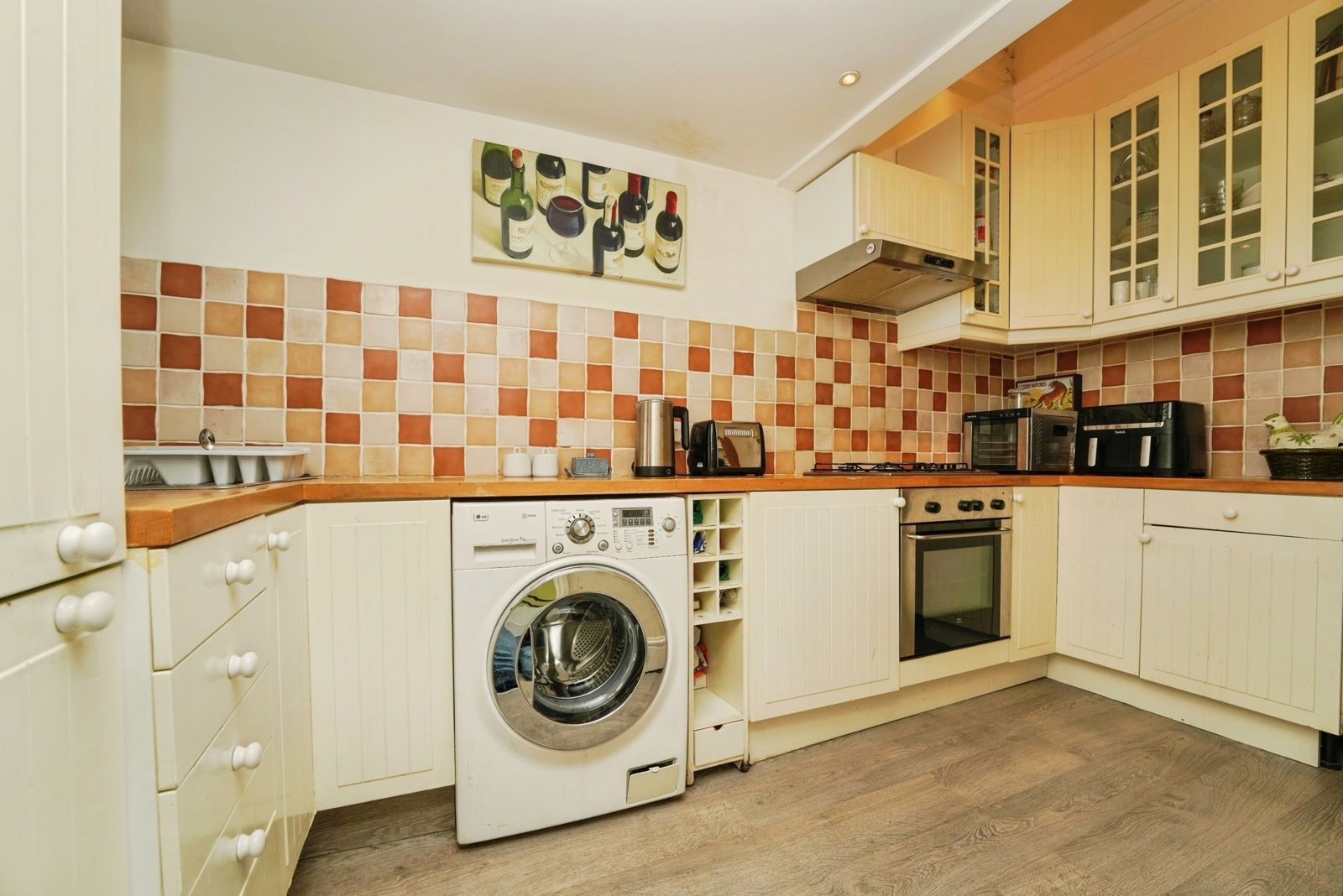 Kitchen from the far end, with washing machine, wooden worktops and cream units